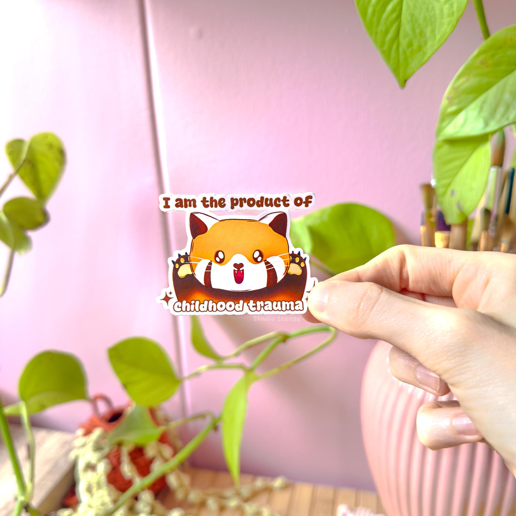 Close-up of a hand peeling and placing the red panda sticker onto a smooth surface near a plant to show size and flexibility. The matte laminated surface and clean die cut edges highlight the durable finish. This funny therapy humor decal applies easily to journals, planners, laptops and water bottles as a playful, relatable mental health joke.