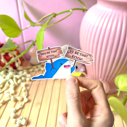 Close-up of a hand peeling and placing the shark sticker onto a smooth surface near a plant to show size and flexibility. The matte laminated surface and clean die cut edges highlight the durable finish. This funny confidence quote decal applies easily to journals, planners, laptops and water bottles as a playful self love reminder.