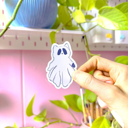 Close-up of a different kawaii ghost kitty sticker being lifted carefully by hand, allowing customers to see every detail of the shape and illustration. The soft white border, clean cut edges, and smooth matte lamination stand out against the warm studio lighting. This photo emphasizes water resistance and durability while keeping the playful pastel goth vibe. A cute spooky cat decal ideal for planners, scrapbooks, laptops, and Halloween-themed stationery collections.