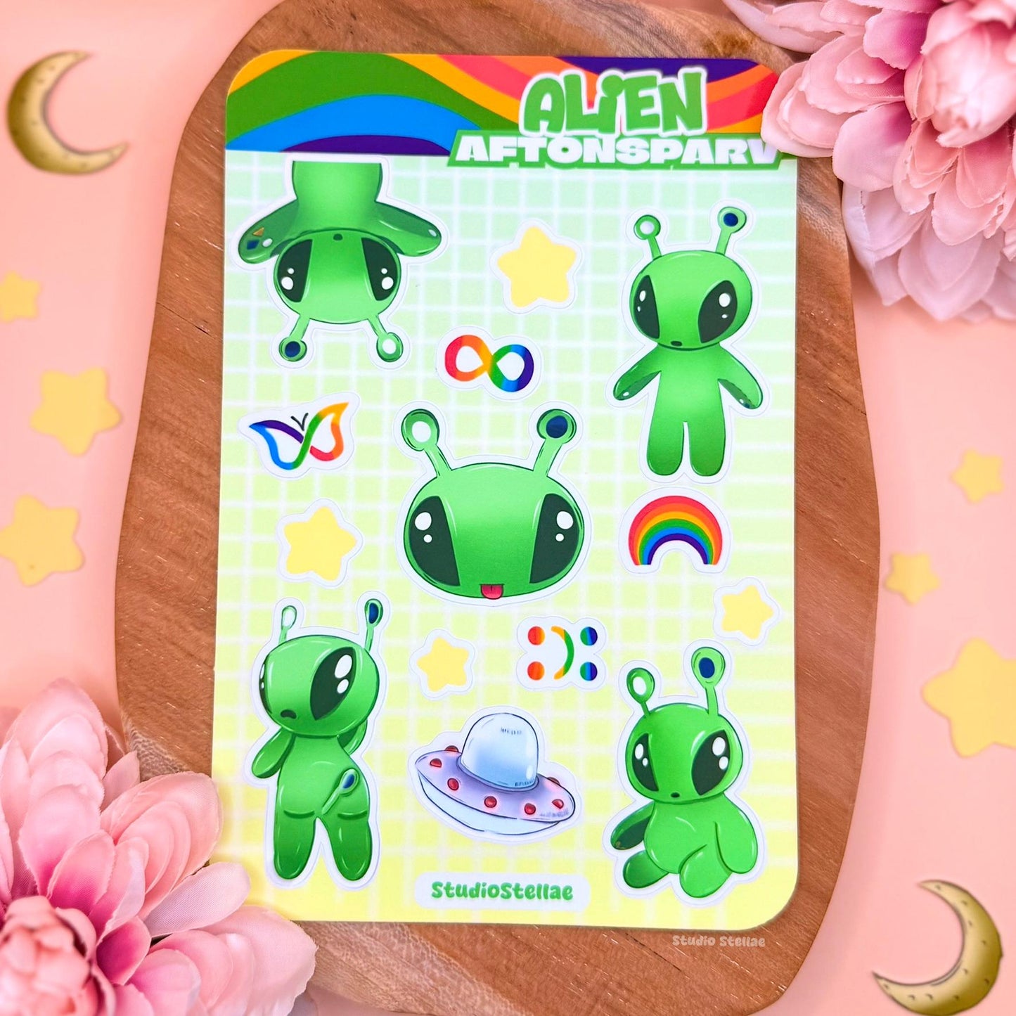 Aftonsparv alien sticker sheet styled on a soft pink background with pastel props, showing the full collection of kawaii green aliens, rainbow motifs, stars, and neurodivergent symbols. This IKEA alien inspired sticker sheet highlights the playful layout and colorful details, perfect for decorating planners, laptops, water bottles, journals, or phone cases while celebrating autism pride, ADHD awareness, and mental health positivity in a cute and gentle way.