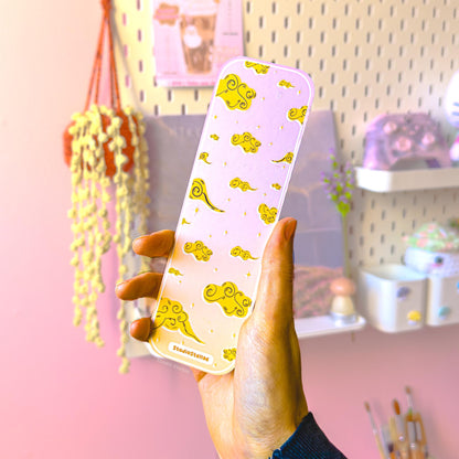 Front and back view graphic of the pastel Andarna-inspired dragon bookmark shown side by side on a pink background, labeled “Front” and “Back.” The front features a golden fantasy dragon surrounded by soft clouds and tiny star accents, while the back shows a complementary pastel design that matches the dreamy aesthetic. The slim rectangular shape, rounded corners, and smooth matte laminated finish are clearly visible, highlighting the double-sided page marker style.