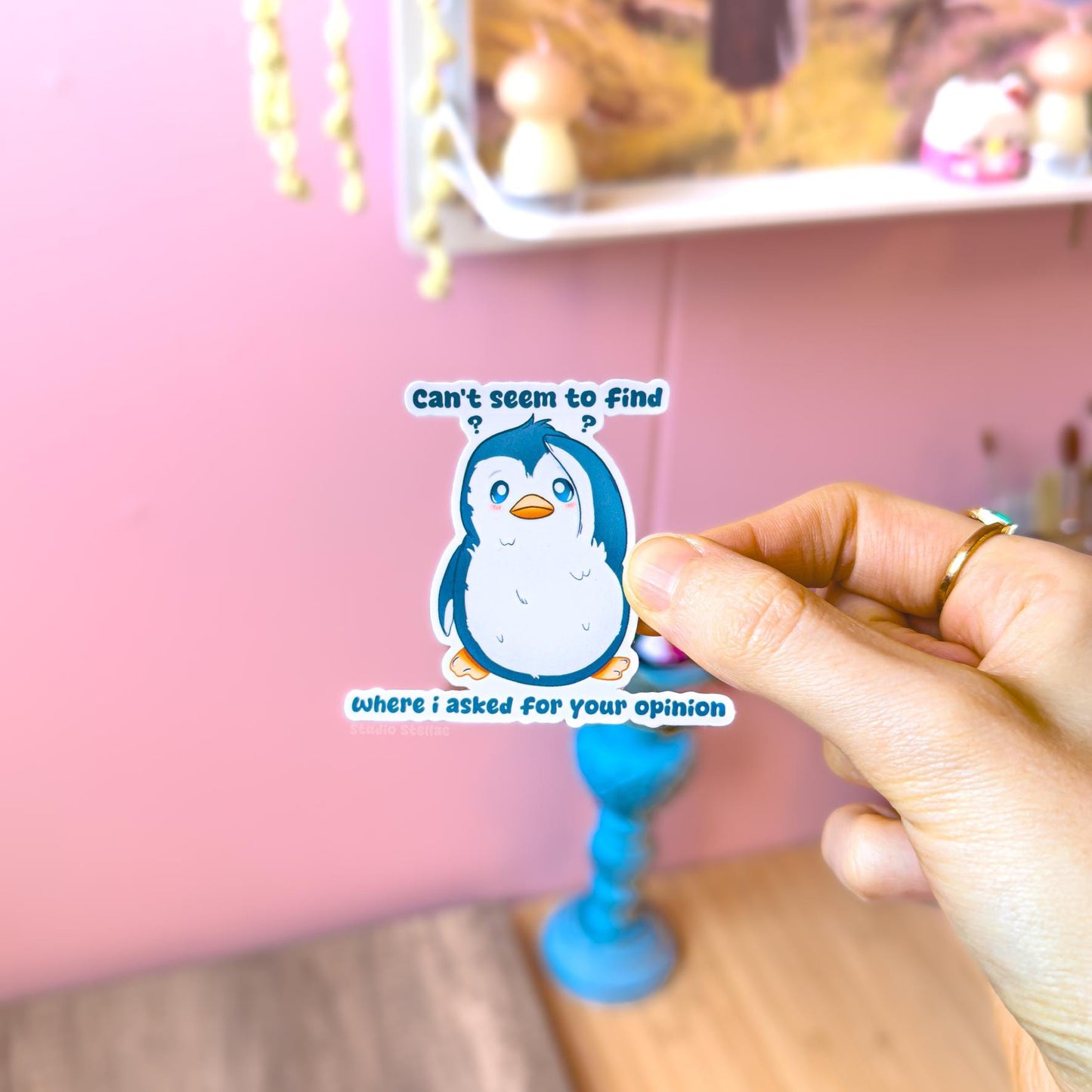 Close-up of a hand holding the blue penguin sticker near green plants in natural light to show true size and color. The fluffy kawaii penguin and the quote “Can’t seem to find where I asked” create playful sarcastic humor in a cute form. This matte laminated vinyl decal works perfectly on laptops, planners, notebooks and water bottles.