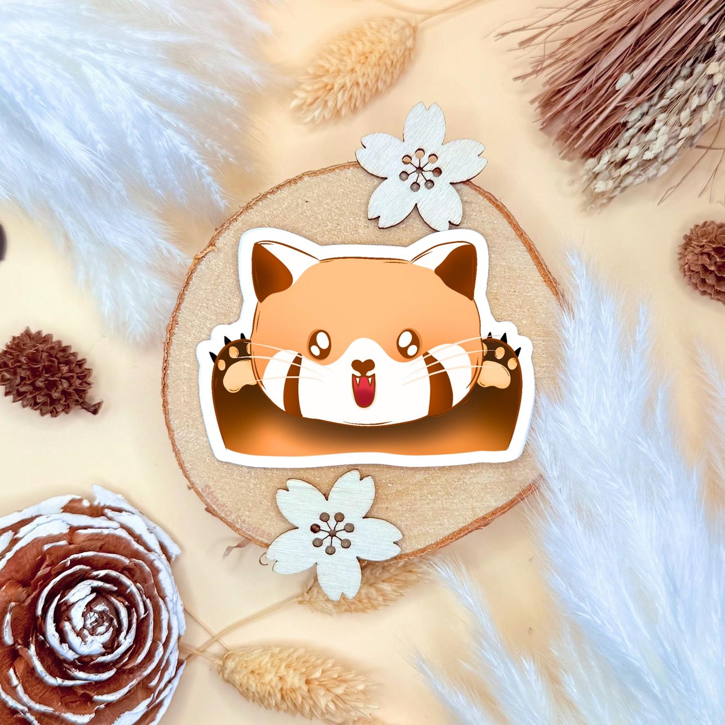 The happy red panda sticker placed on a warm neutral flat lay with dried flowers and textured props, styled like a gift or scrapbook scene. The composition highlights the sticker’s shape, thickness and finish while showing how it complements cozy stationery aesthetics. A decorative product shot that inspires creative uses for scrapbooking, journaling and laptop personalization.