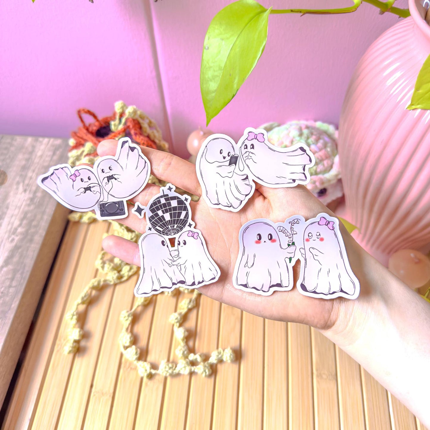 All ghost couple stickers scattered together on a wooden desk near green plants, showing the complete set in natural light. Multiple poses like cuddling, gaming and dancing create a playful little love story. Perfect for decorating planners, scrapbooks, laptops and water bottles with soft pastel spooky cute Halloween charm.