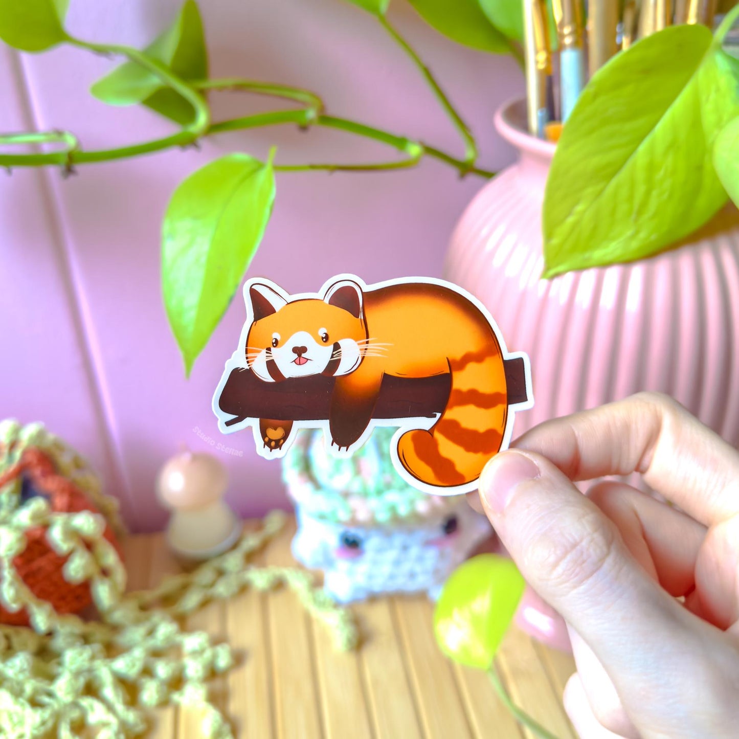 Hand holding the sleepy red panda sticker with a relaxed, curled-up pose that captures cozy, low-energy days. The soft colors and rounded chibi style give it a comforting feel, while the matte laminate reduces glare. This close-up emphasizes the “lazy mood” design, ideal for planners, notebooks or water bottles and relatable for anyone who loves cute animal humor and calm aesthetics.