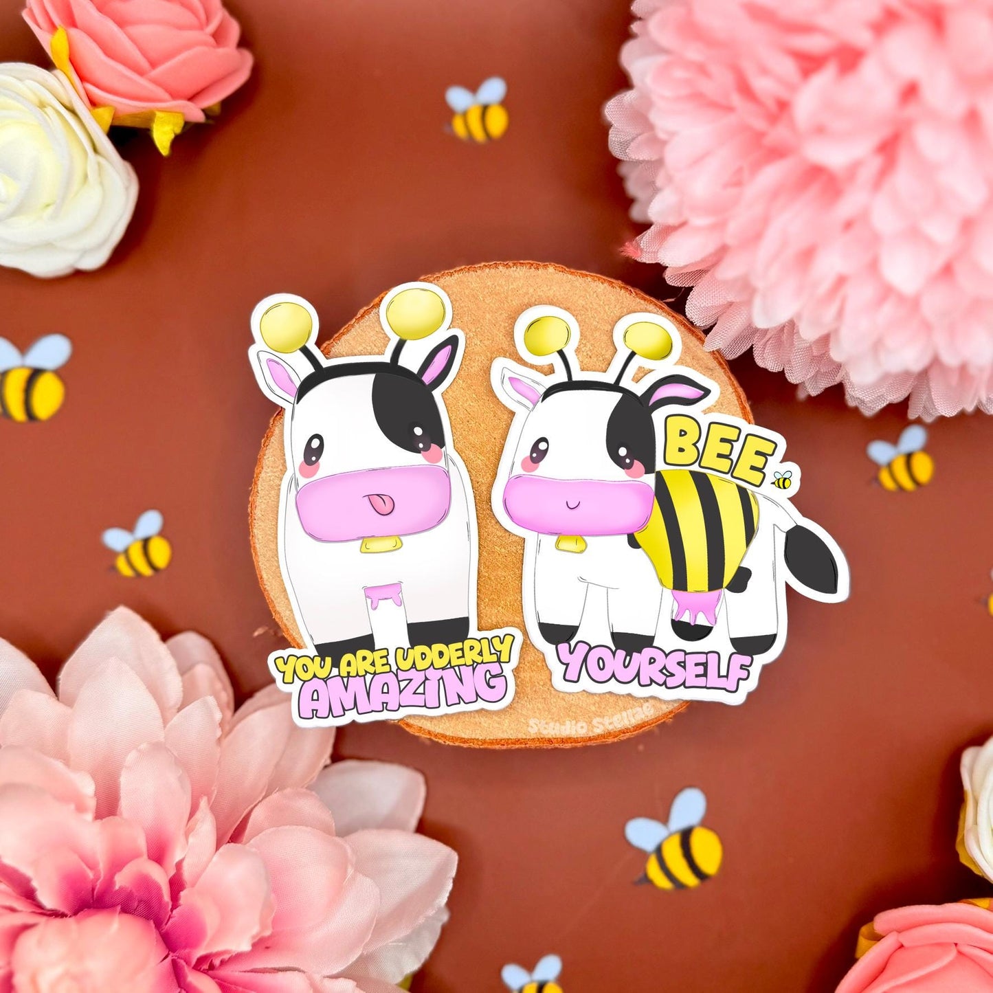 Cute kawaii cow dressed as a bumblebee sticker set featuring soft pastel colors, blushing cheeks, and a playful expression. One sticker reads “You are udderly amazing” and the other says “Bee yourself,” promoting self-acceptance, identity, and kindness. The stickers are styled on a warm-toned background with pink flowers and tiny bees around them. Perfect for decorating journals, laptops, planners, water bottles, or as an encouraging and inclusive gift that spreads positivity.