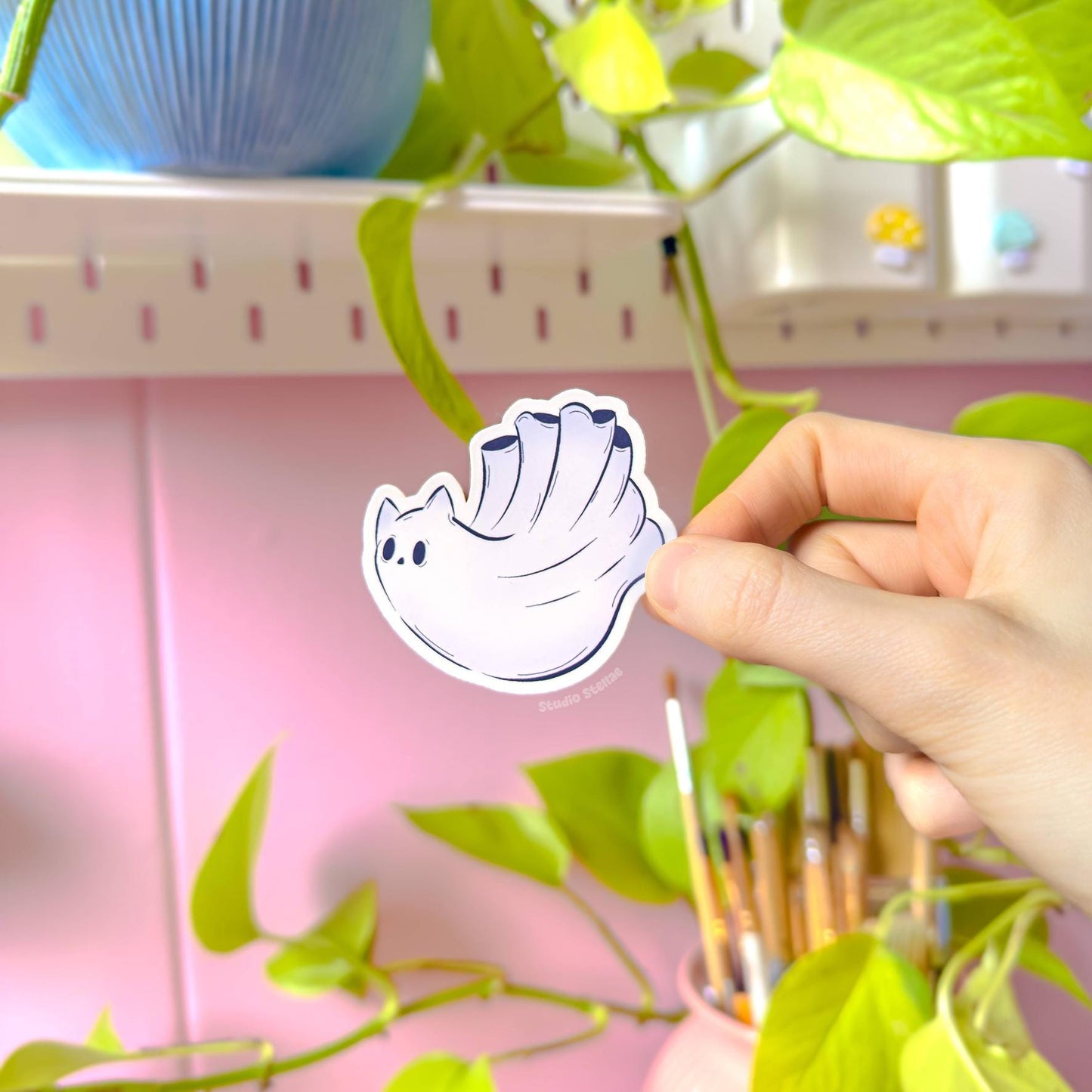 Detailed hand-held photo of another ghost cat sticker design, photographed in warm daylight with soft greenery in the background for a fresh, cozy look. The expressive chibi face and gentle pastel tones give this spooky kitty a sweet personality while still fitting the Halloween theme. The image clearly shows sticker size, thickness, and the silky matte finish. Handmade, durable, and perfect for decorating everyday items with cute paranormal cat art.