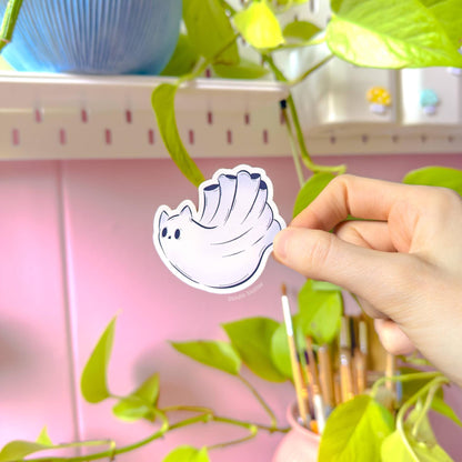 Detailed hand-held photo of another ghost cat sticker design, photographed in warm daylight with soft greenery in the background for a fresh, cozy look. The expressive chibi face and gentle pastel tones give this spooky kitty a sweet personality while still fitting the Halloween theme. The image clearly shows sticker size, thickness, and the silky matte finish. Handmade, durable, and perfect for decorating everyday items with cute paranormal cat art.