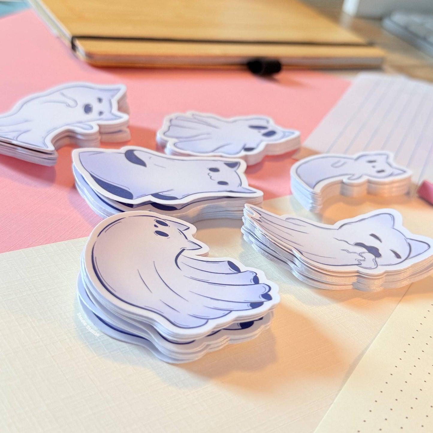 Close-up of several ghost kitty stickers stacked neatly on top of each other to demonstrate thickness, durability, and material quality. The matte laminated surface softly reflects the light, revealing smooth edges, crisp die-cuts, and sturdy sticker paper that won’t easily bend or tear. This detail shot reassures customers about long-lasting use while keeping the cute pastel goth cat aesthetic. Perfect for highlighting the premium handmade feel of each spooky decal.