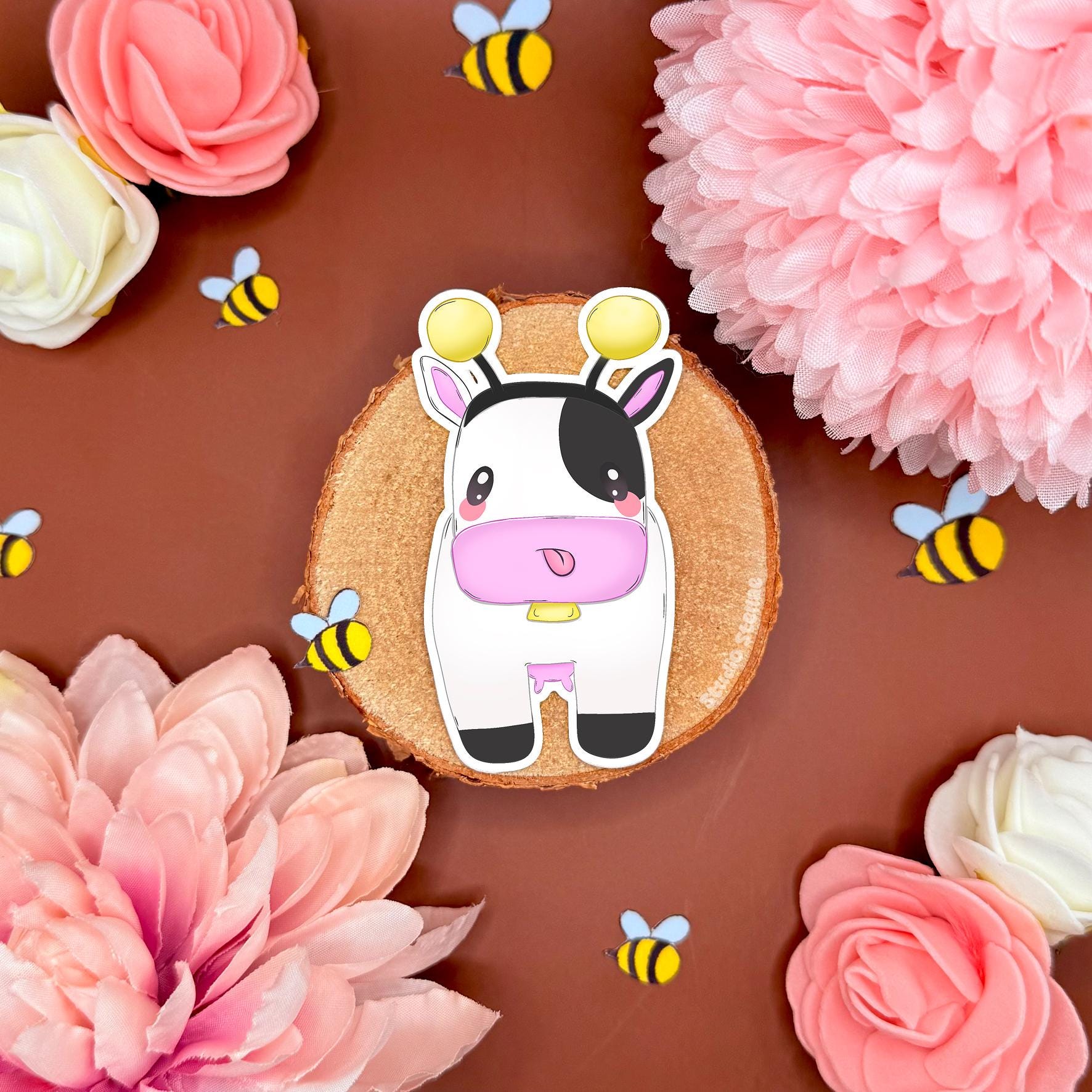 Close up of the upright bee cow sticker on a warm brown background with pink flowers and tiny bee confetti. Shows the chibi cow’s cute expression and bee costume details clearly, including stripes and little wings. This image emphasizes the smooth matte finish and clean cut edges, helping customers picture it as a cozy farm vibe sticker for notebooks, planners, laptops, or water bottles—great as a nostalgic gamer gift.