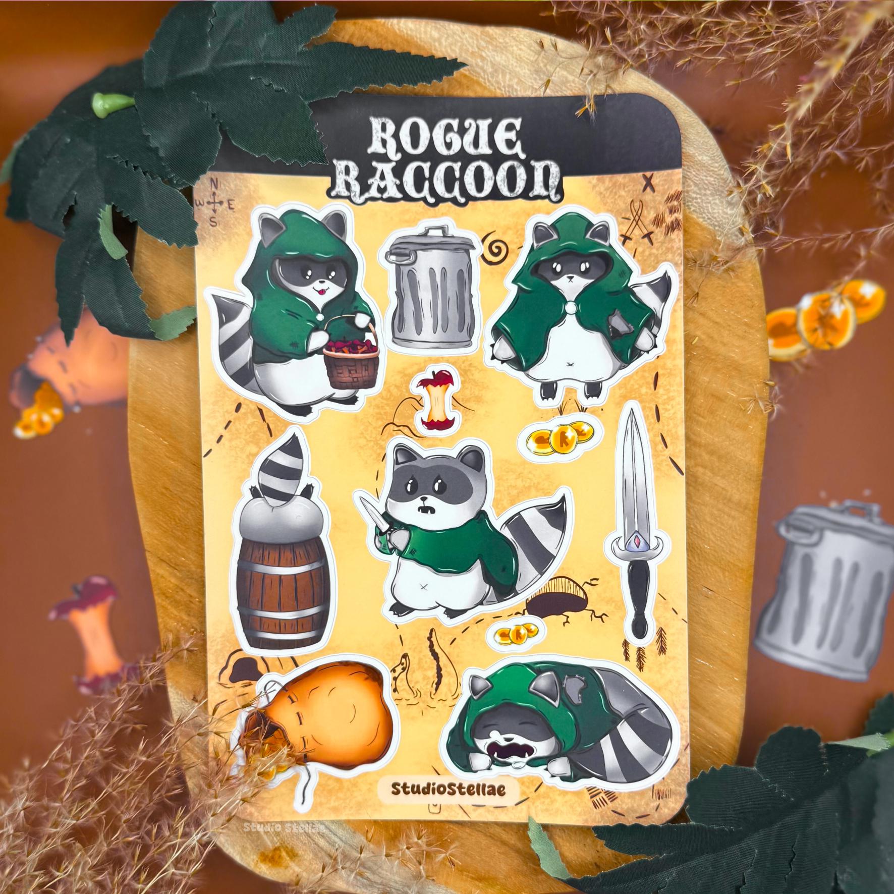 Rogue Raccoon sticker sheet styled in a cozy fantasy scene with autumn leaves, warm lighting, and soft textures. The sheet shows chibi raccoon rogue characters wearing green cloaks, holding loot and daggers, alongside accessories like gold coins, a trash can, barrel, treasure sack, and fantasy props. The matte laminated surface and rounded corners are visible, creating a cute DnD and tabletop RPG inspired aesthetic perfect for raccoon lovers and fantasy sticker collectors.