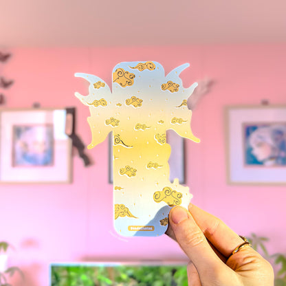 Hand holding the pastel dragon bookmark in front of a soft pink wall with framed pictures in the background. The bookmark’s dreamy cloud-and-stars color palette and golden cloud accents are clearly visible, showing the overall size and shape in hand. This image highlights the laminated finish and whimsical fantasy design inspired by Fourth Wing and the Empyrean series, ideal for romantasy readers and BookTok book lovers.