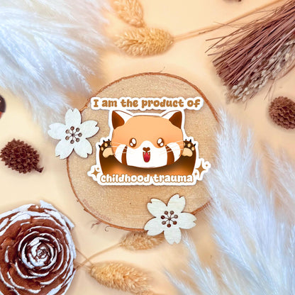 Cute red panda chibi sticker styled in a warm cozy flat lay with dried wheat and soft neutral textures. The kawaii red panda lies cutely with the funny dark humor quote “I am the product of childhood trauma,” blending adorable cartoon art with relatable therapy humor. This handmade matte laminated vinyl decal adds personality to laptops, planners, journals and water bottles as a playful mental health joke.