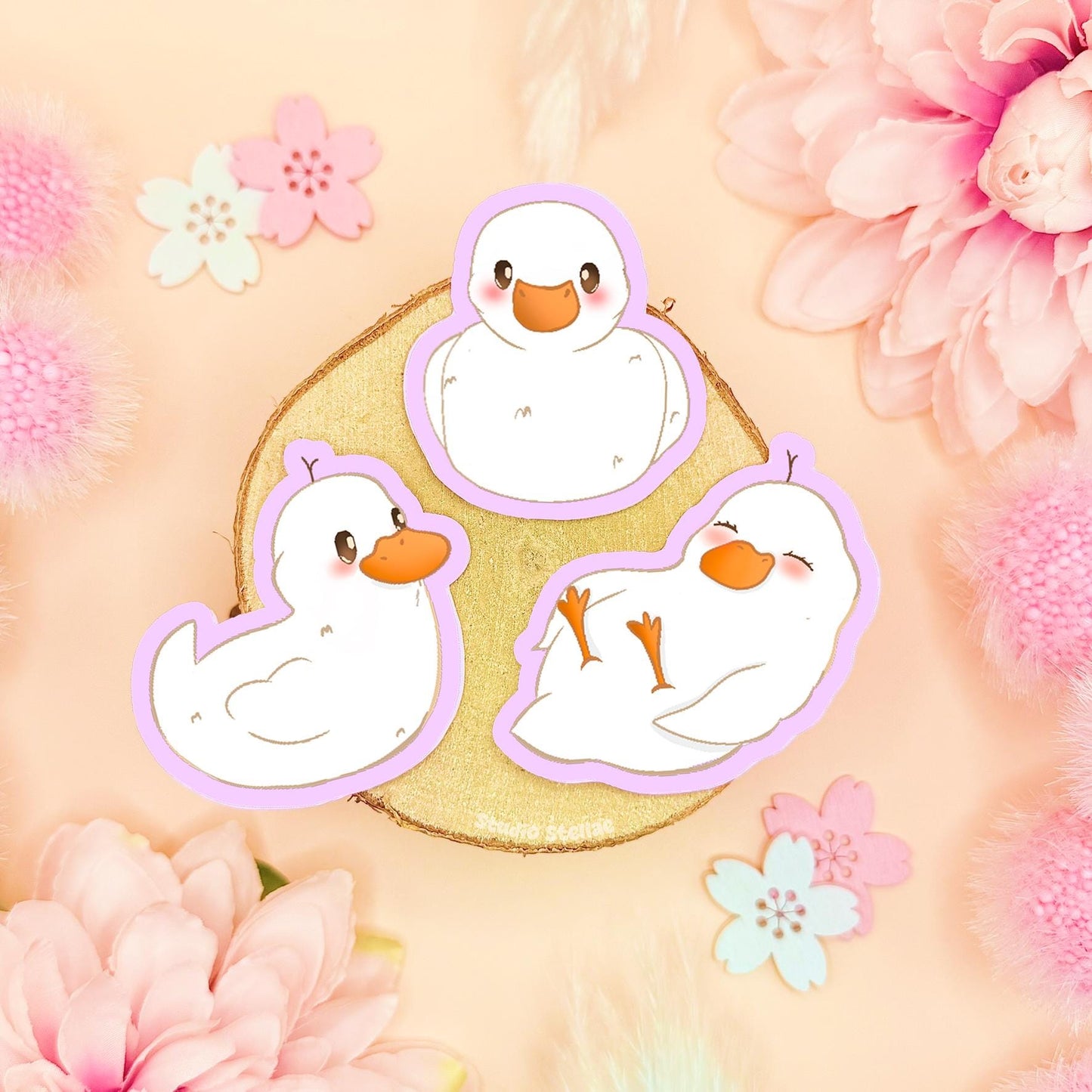 Baby duck sticker set featuring three tiny pastel duckling stickers arranged on a soft pink background with flowers and decorative props. This kawaii duck sticker pack shows cute white duck characters in different poses, highlighting their matte finish and soft colors. Handmade waterproof baby duck decals perfect for decorating laptops, planners, journals, scrapbooks, or water bottles, and a sweet gift for duck lovers, stationery fans, and anyone who loves cozy pastel animal stickers.