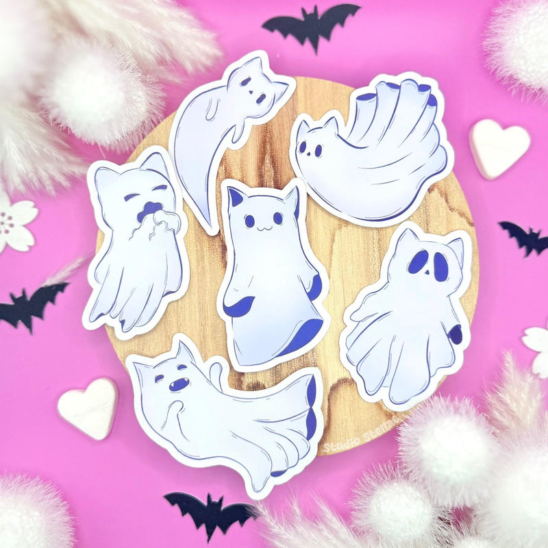 Full Ghost Kitty sticker set displayed on a soft pastel pink background scattered with tiny hearts, creating a cute yet slightly spooky pastel goth aesthetic. Six kawaii ghost cats float together, each with its own playful, sleepy, or mischievous expression. This main image shows the entire Halloween sticker pack at a glance while highlighting clean die-cut edges, vibrant pastel colors, and a smooth matte laminated finish. Perfect for planners, journals, laptops, and cozy seasonal Sticker lovers