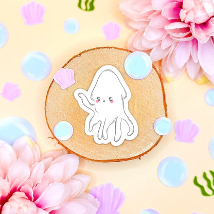 Close-up of the white chibi squid sticker styled on a pastel background with flowers and soft bubbles, highlighting its rounded shape, gentle expression and soft kawaii aesthetic. The matte laminated surface keeps colors vibrant and protects from scratches and water. A sweet ocean animal decal perfect for decorating laptops, planners, journals and water bottles with cozy sea life vibes.