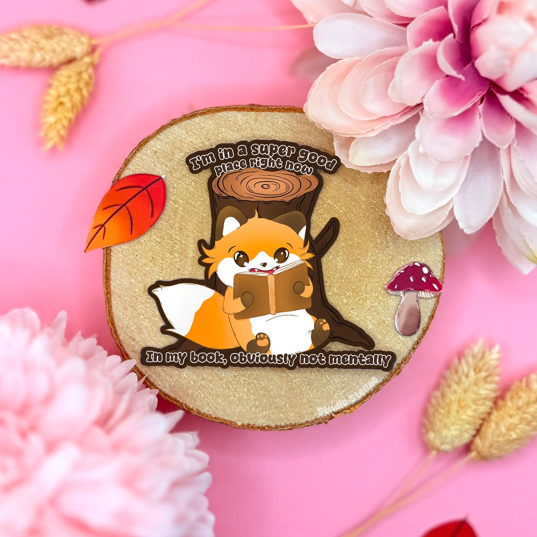Bookish fox Kindle sticker styled in a soft pastel flat lay with pink flowers and warm cork textures. The cute cozy fox curls up with a book beside the funny mental health reading meme quote, “I’m in a super good place right now… in my book.” This handmade matte laminated decal is perfect for Kindles, laptops, water bottles, planners and journals, making it a relatable introvert bookworm gift for readers who escape into stories.