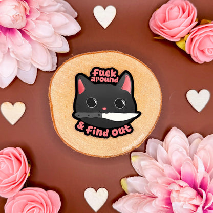 Funny black cat meme sticker styled in a soft flat lay with pink flowers and warm cork textures. The sassy chibi kitty stares with attitude beside the bold “fuck around & find out” FAFO quote, blending cute kawaii cat art with sarcastic adult humor. This handmade matte laminated vinyl decal adds chaotic gremlin energy to laptops, planners, notebooks and water bottles as a playful warning sticker.