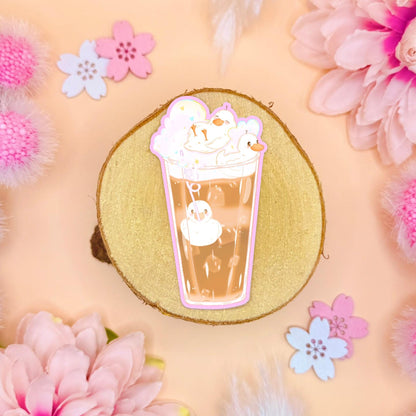 Cute duck sticker styled in a soft pastel flat lay with pink flowers and warm cork textures. The design shows a cozy glass of hot chocolate filled with whipped cream and marshmallows shaped like tiny happy ducks floating on top. This kawaii cocoa duck art feels warm and whimsical, blending cute animal illustration with cozy winter vibes. Handmade matte laminated decal, perfect for planners, journals, laptops and water bottles or as a sweet gift for duck lovers.