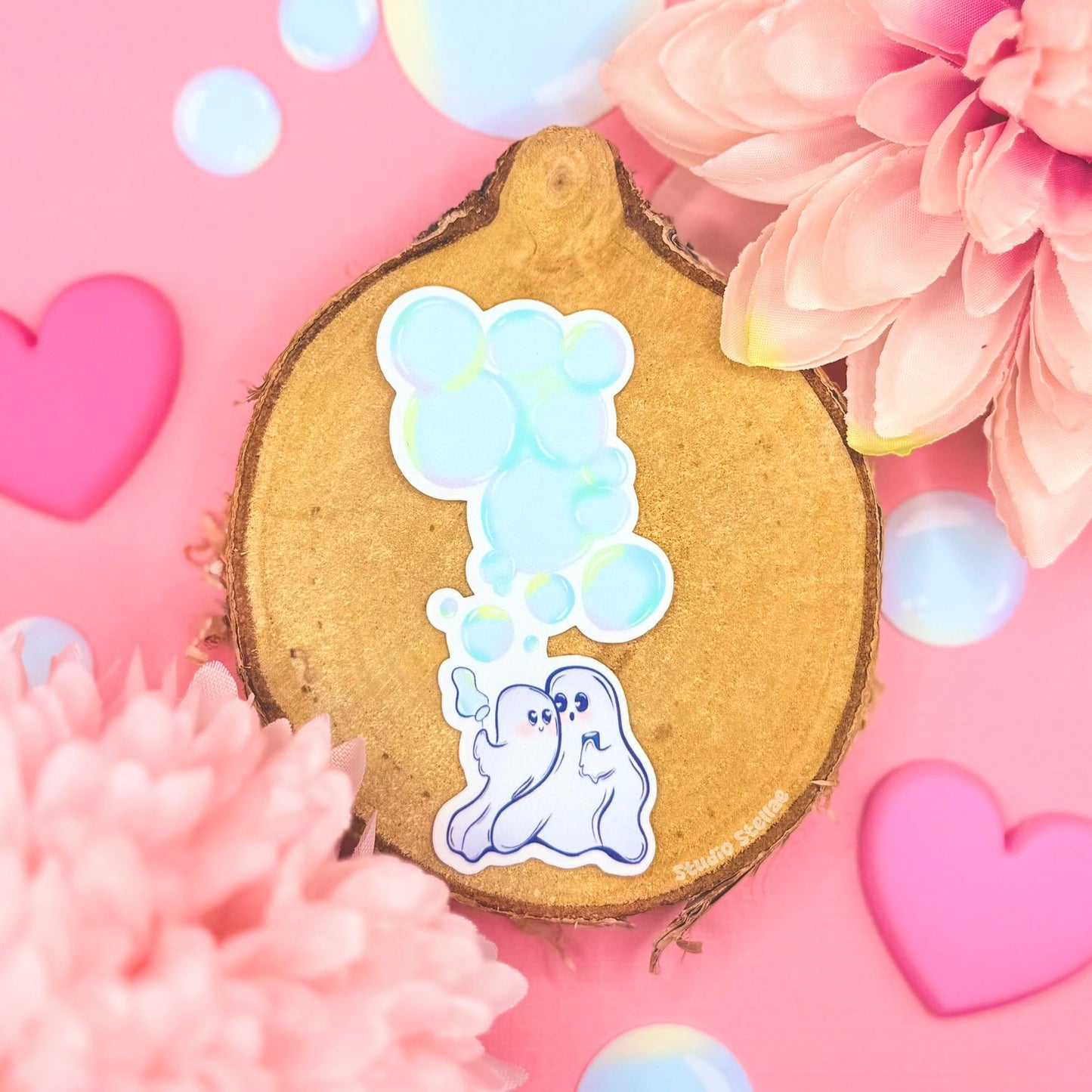 Cute ghost couple sticker styled in a soft pastel flat lay with pink flowers, hearts and warm cork textures. Two tiny kawaii ghosts float together holding hands and blowing bubbles, creating a sweet pastel goth and romantic Halloween vibe. This handmade matte laminated vinyl decal blends spooky cute charm with cozy love energy, perfect for decorating journals, planners, laptops and water bottles or gifting to your partner.