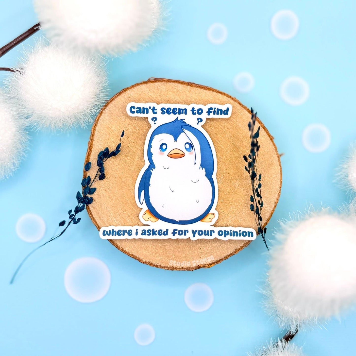 Sarcastic penguin sticker styled in a soft pastel flat lay with fluffy pom poms and cork textures. The cute blue penguin stands with a sassy expression beside the quote “Can’t seem to find where I asked,” blending adorable kawaii animal art with snarky passive-aggressive humor. This handmade matte laminated vinyl decal is perfect for decorating laptops, planners, notebooks and water bottles.