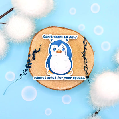 Sarcastic penguin sticker styled in a soft pastel flat lay with fluffy pom poms and cork textures. The cute blue penguin stands with a sassy expression beside the quote “Can’t seem to find where I asked,” blending adorable kawaii animal art with snarky passive-aggressive humor. This handmade matte laminated vinyl decal is perfect for decorating laptops, planners, notebooks and water bottles.