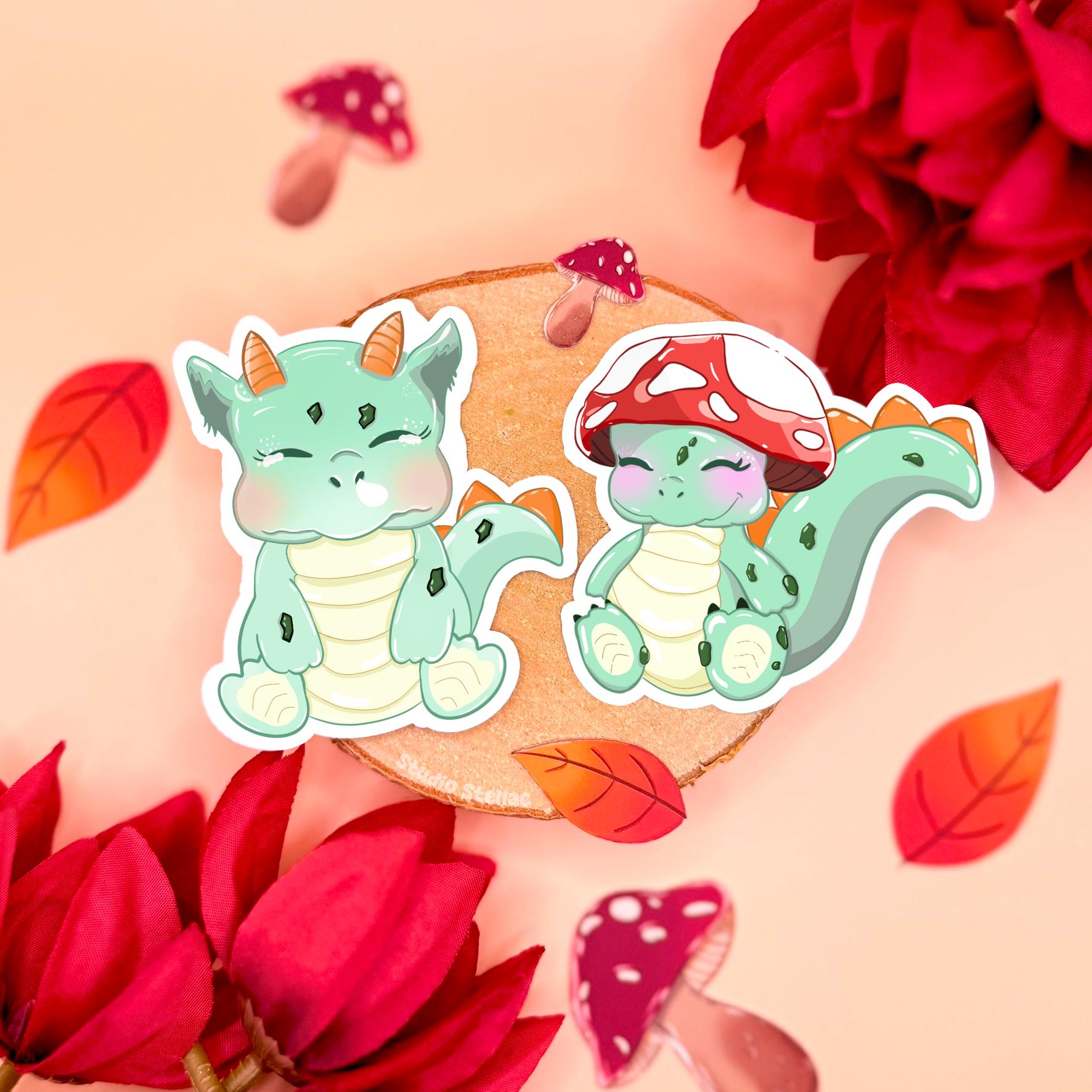 Cute baby dinosaur sticker set styled in a soft pastel flat lay with cork, red flowers and cozy cottagecore props, showing both chibi dinos side by side. One sleepy mint green dinosaur sits calmly while the smaller friend wears an adorable red mushroom hat. These kawaii cottagecore dino stickers are matte laminated, waterproof and perfect for decorating planners, journals, laptops and water bottles, making a sweet fantasy stationery gift for cute trinket lovers.