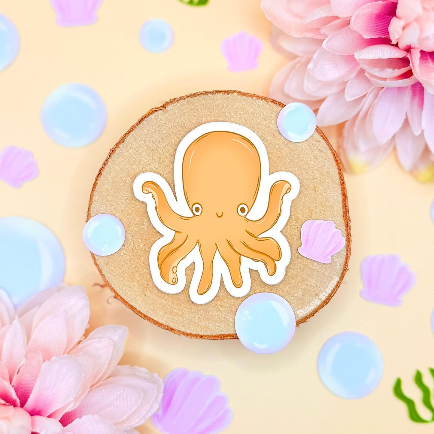 Close-up of the small yellow chibi octopus sticker placed on cork with pastel flowers and bubble accents, showing fine details, smooth matte laminate and clean cut outline. The cheerful ocean creature adds a playful pop of color to planners, journals and water bottles and pairs perfectly with the shark and squid designs in the set, making it a cute and fun sea life decoration.