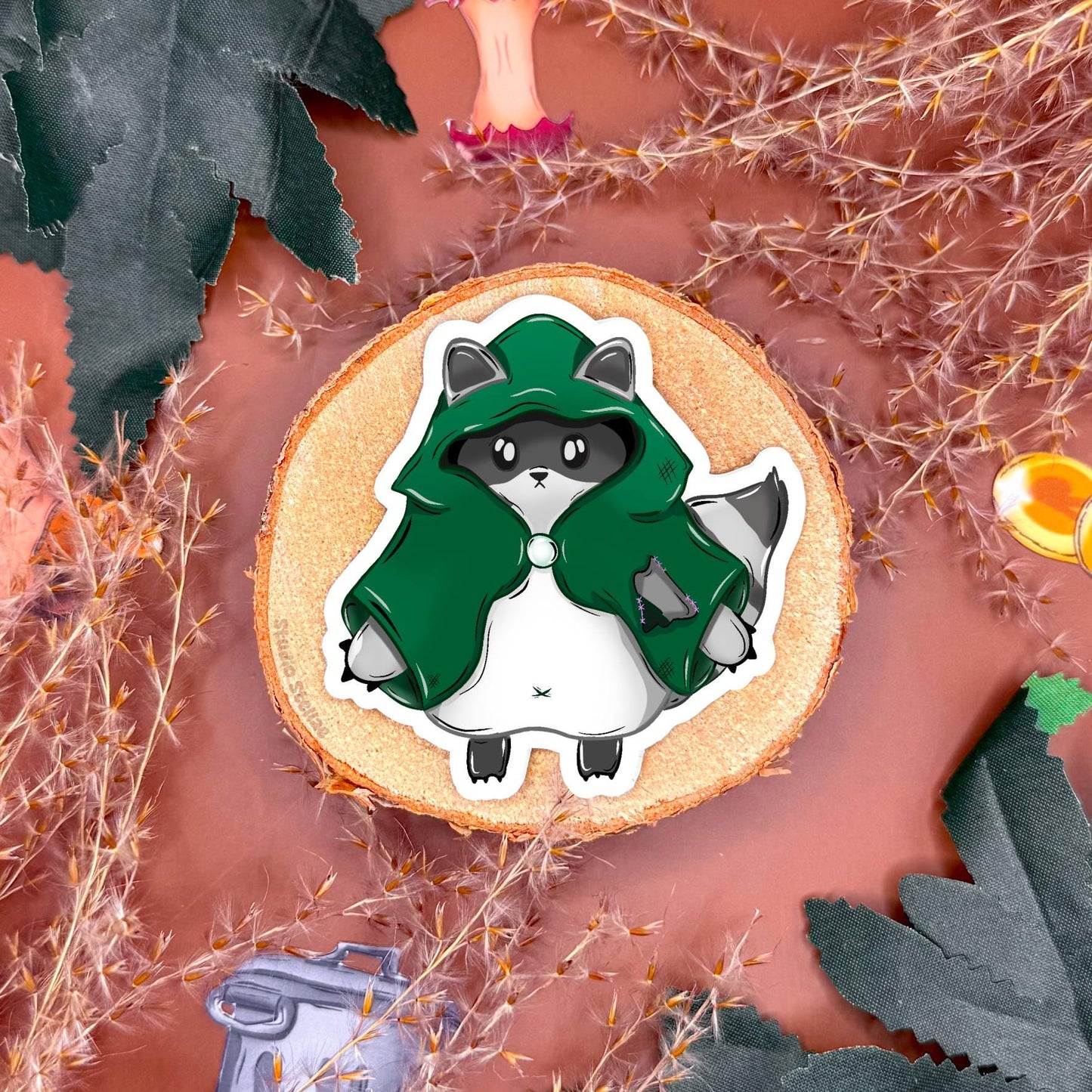 Close up of a standing raccoon rogue sticker displayed on a fantasy themed surface, showing character outfit details and expressive pose. The chibi trash panda looks ready for adventure, embodying playful tabletop RPG energy and sneaky rogue personality. Highlights vibrant colors, clean cut edges, and smooth matte lamination, demonstrating how this DnD sticker adds charm to dice boxes, laptops, journals, or water bottles and makes a fun nerdy gift.