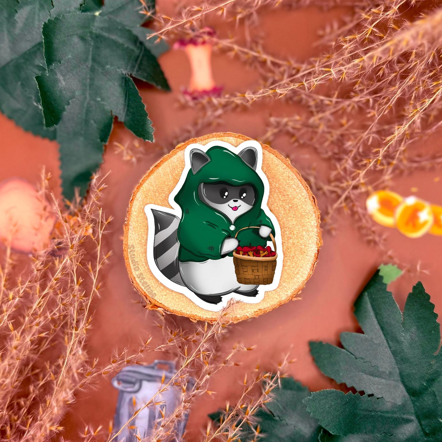 Close up of a sticker featuring a basket filled with slightly rotten apples, styled on a fantasy tabletop background with cozy props and warm lighting. This design adds environmental storytelling to the rogue raccoon DnD sticker set, evoking classic tabletop RPG loot and camp scenes. The image highlights illustration details, texture, and matte finish, showing how this fantasy themed sticker can be used to decorate gaming accessories, planners or laptops for players who love campaign aesthetics.