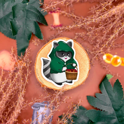 Close up of a sticker featuring a basket filled with slightly rotten apples, styled on a fantasy tabletop background with cozy props and warm lighting. This design adds environmental storytelling to the rogue raccoon DnD sticker set, evoking classic tabletop RPG loot and camp scenes. The image highlights illustration details, texture, and matte finish, showing how this fantasy themed sticker can be used to decorate gaming accessories, planners or laptops for players who love campaign aesthetics.