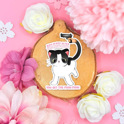Cat With Gun sticker displayed in a soft pastel flat lay with pink flowers and cork textures. The cute white chibi kitten holds a tiny toy gun beside the funny meme quote “You mess with the meow meow, you get the peow peow.” This handmade matte laminated vinyl decal blends kawaii cat art with internet humor, perfect as a laptop sticker, water bottle decal, journal decoration or gift for cat lovers and meme fans.